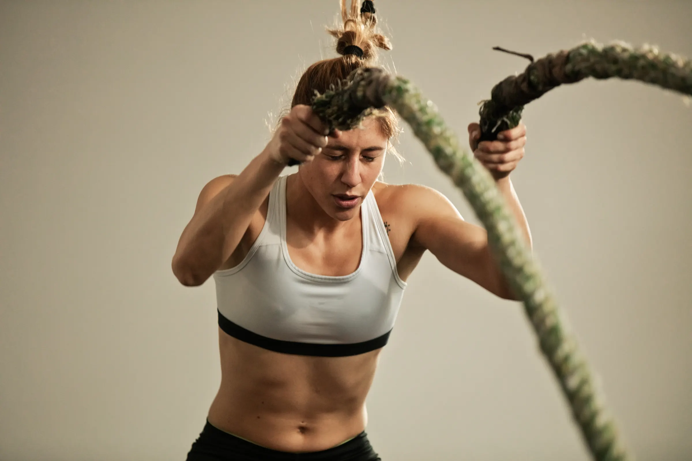 Athlete doing a battle rope workout, focused, against a neutral background