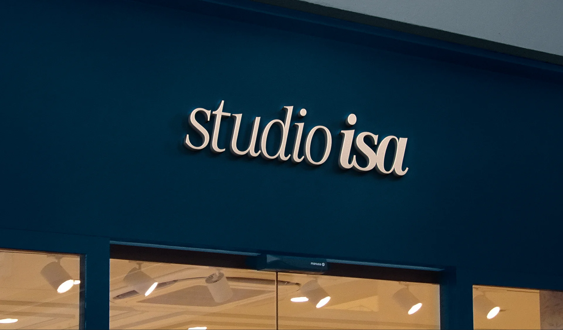 Studio facade in deep teal with the studio isa logotype in relief, over a window with lit glass doors