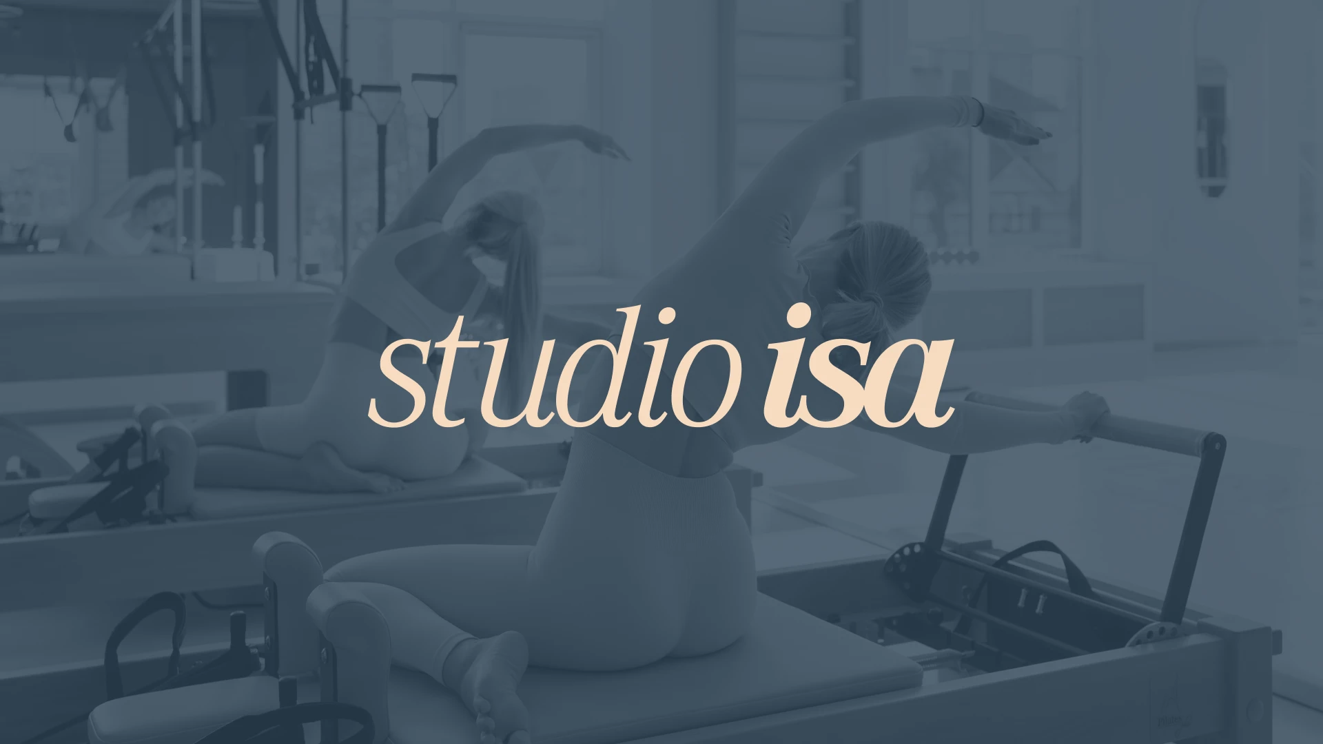 Two women practicing pilates on reformer machines, in blue tones, with the studio isa logotype in beige at the center