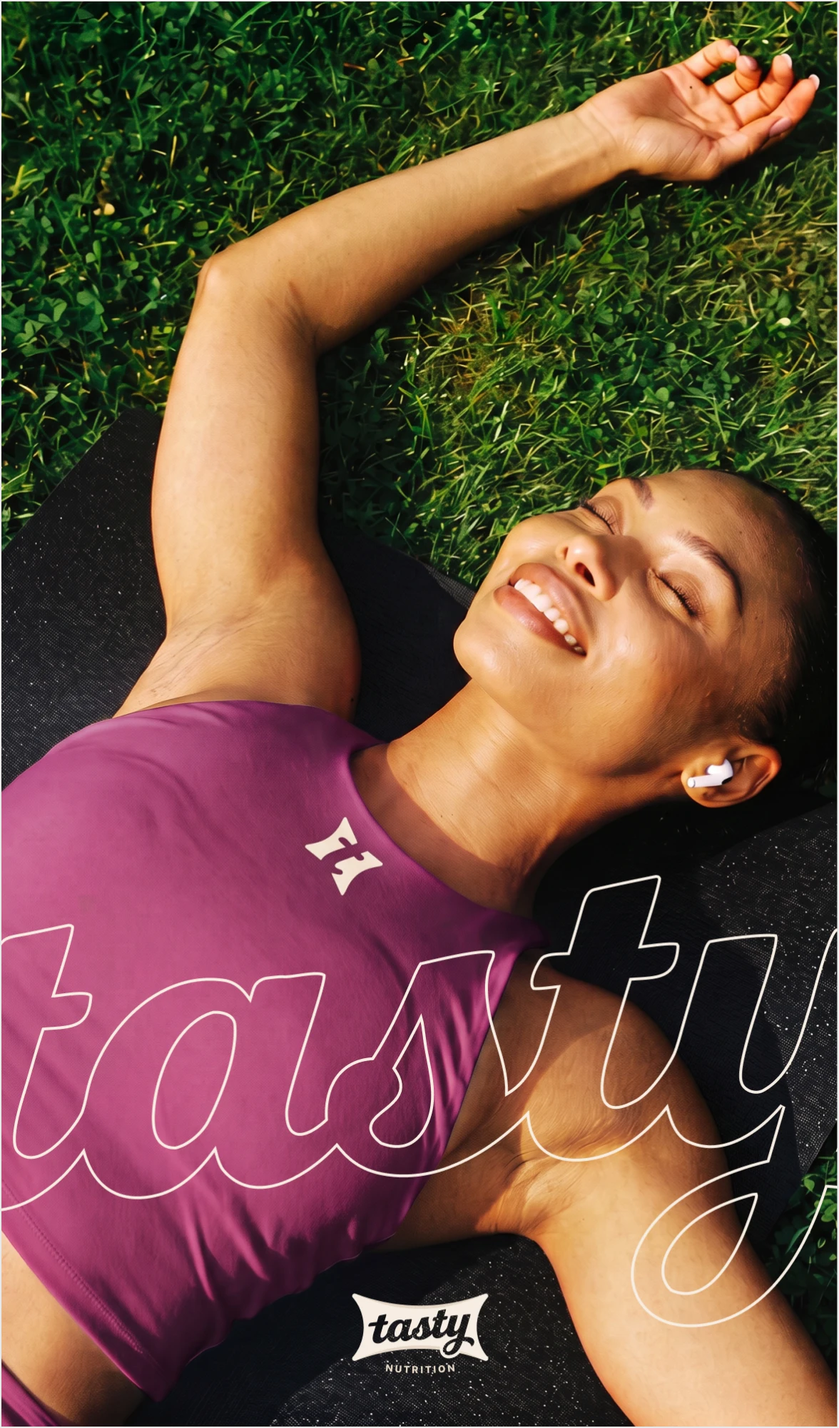 Smiling woman lying on the grass in a purple top, with the outlined tasty lettering over her